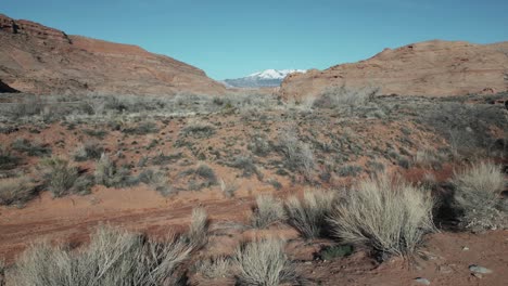 Vuelo-Bajo-De-Drones-Sobre-El-árido-Paisaje-De-Utah-Con-Vistas-Lejanas-A-Las-Montañas-Nevadas