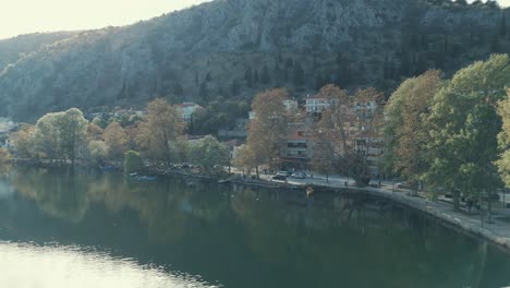 Drohnenflug-Zu-Einem-Dorf-Auf-Einem-Hügel-In-Europa,-Grüne-Bäume,-Sonniges-Wetter,-Blauer-See,-Malerische-Berge,-Griechenland,-4K-Video