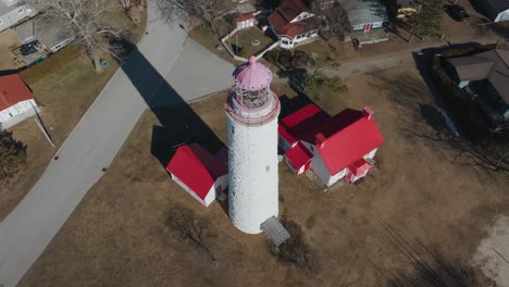 A-historic-white-lighthouse-with-red-roofs-in-a-residential-area-on-a-sunny-day,-showcasing-the-unique-architectural-details,-aerial-view
