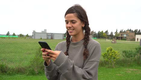 Young-brunette-woman-texts-on-phone-and-smiles-outdoors-in-rural-town