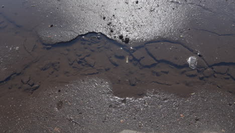 Self-Created-Stream-of-Water-on-Sandy-and-Muddy-Brown-Pavement,-Showcasing-the-Dangers-of-Poorly-Maintained-Public-Road