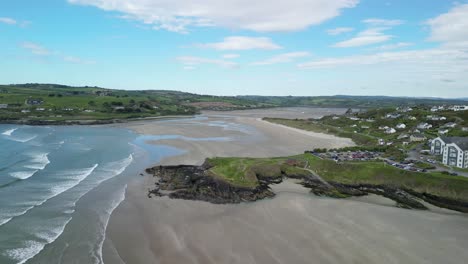 Imágenes-Aéreas-Sobre-La-Playa-De-Arena-De-Inchidoney-Durante-La-Marea-Baja-Con-Olas-Y-Panorama-De-Colinas-Verdes,-Pueblo-Con-Casas-Y-Costa-Escarpada