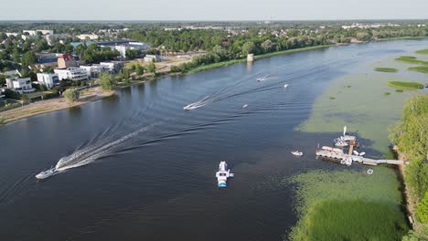 Boats-motor-down-natural-Parnu-River-in-city-of-Parnu,-western-Estonia