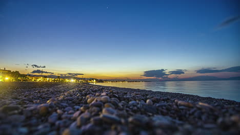 Pebbles-and-coastal-town-with-night-lights,-low-angle-time-lapse-view