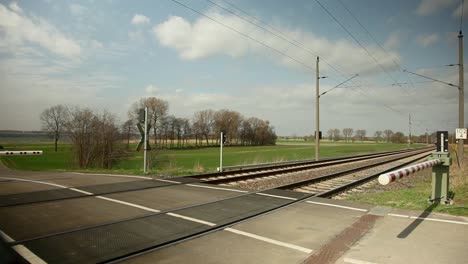 Red-train-speeding-past-a-rural-level-crossing-during-a-sunny-day,-clear-sky,-dynamic-motion-blur