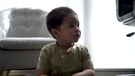 Young-boy-watches-TV-intently,-sitting-indoors-with-natural-light,-relaxed-yet-focused-expression