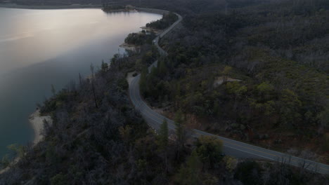 Aerial-pan-up-over-a-road-that-follows-the-contours-of-Whiskeytown-Lake-in-Northern-California-with-a-truck-driving-on-it