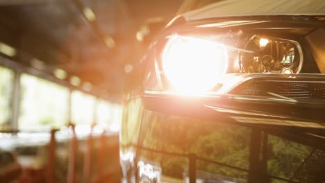 Faro-De-Coche-Encendido-En-Un-Garaje-Con-Poca-Luz-Y-Un-Fondo-Iluminado-Por-El-Sol,-Con-Una-Toma-Panorámica