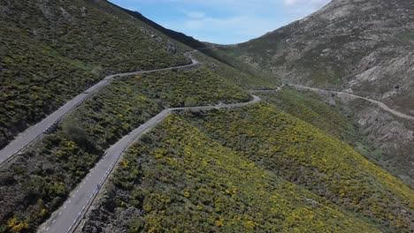 Vuelo-Ascendente-Con-Un-Dron-Visualizando-Una-Carretera-De-Montaña-En-Su-Tramo-Final-Donde-Se-Proyecta-La-Sombra-De-Una-Nube-Todo-Es-Con-Una-Alta-Planta-De-Montaña-Amarilla-Puerto-De-Mijares-Avila-España