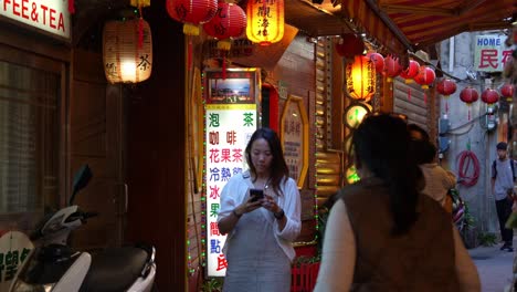 Family-taking-photos-in-the-narrow-alleyway-of-Jiufen-Old-Street-with-light-up-red-lanterns-along-the-laneway,-a-popular-tourist-attraction-in-Taiwan