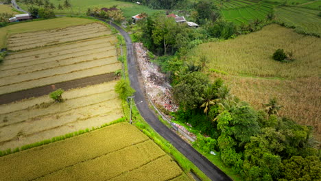 Burning-garbage-pile-next-to-road-in-rural-agricultural-Bali-landscape,-drone