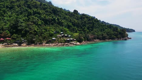 Island-Hill-Huts-in-lush-Jungle-fores,-emerald-waters-lagoon