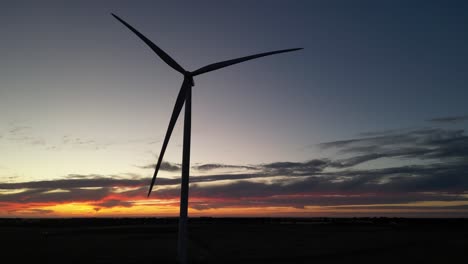 Silhouette-of-rotating-wind-turbine-on-farm-field-during-golden-sunset