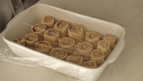 Caucasian-male-chef-covering-homemade-cinnamon-rolls-in-ceramic-baking-tray