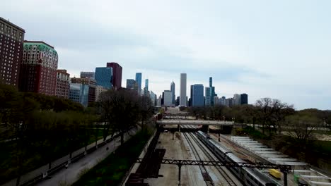 FPV-aerial-drone-footage-of-a-drone-flying-behind-a-train-through-the-train-yard-then-turning-180-into-a-city-park-during-daylight-the-city-statue-stands-tall-on-the-hill