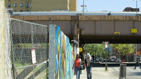 La-Gente-Pasa-Por-Un-Terreno-Baldío-En-Harlem,-Nueva-York,-Con-Un-Tren-Pasando-Por-Encima