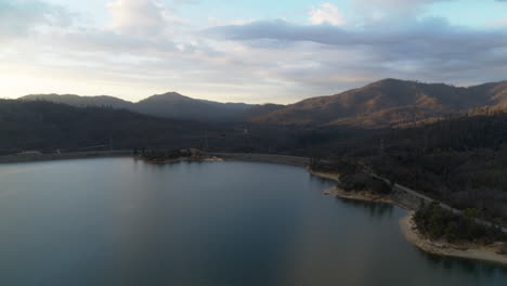 Flyover-of-the-southern-portion-of-Whiskeytown-Lake-with-mountains-and-sunrise-clouds-in-the-background