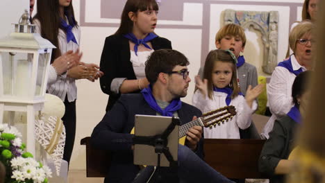 Guitarist-performing-at-a-Spanish-communion-ceremony,-surrounded-by-attentive-children-and-adults
