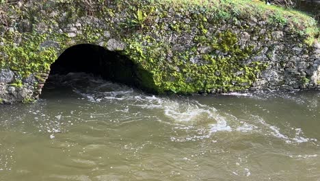 Agua-Que-Fluye-Rápidamente-A-Través-De-Un-Desagüe-En-Un-Puente-De-Piedra