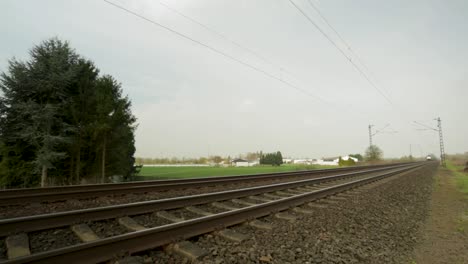 Tren-De-Carga-Borroso-Acelerando-A-Lo-Largo-De-Vías-Rodeadas-De-Vegetación,-Día-Nublado