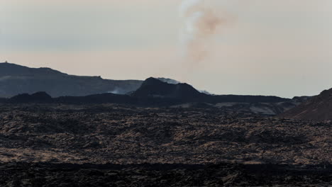 Smoke-rising-from-Grindavik-volcano-against-a-stark,-barren-landscape-at-dusk