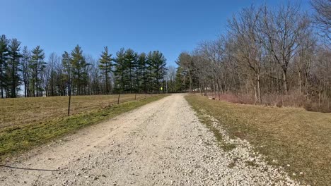 POV---Driving-a-trail-vehicle-on-graveled-lane-and-turning-onto-groomed-trail-through-timber-that-leads-to-a-home