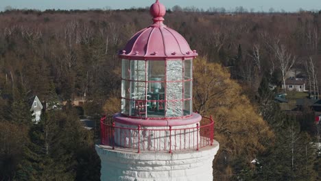 Aerial-shot-of-a-vibrant-pink-lighthouse-with-lush-greenery-and-residential-background,-sunny-day