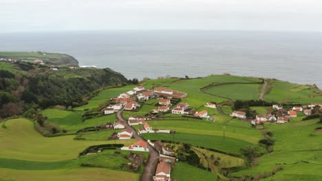 Drone-footage-of-lush-green-volcanic-island-countryside-with-homes-and-highway-near-ocean-bluffs-on-foggy-evening-on-the-Azores-Sao-Miguel-Island