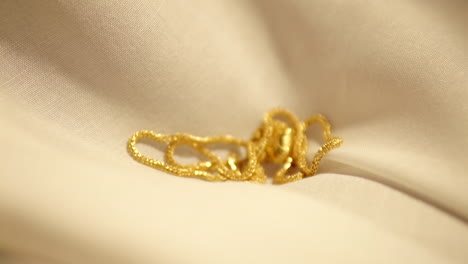 Wunderschöne-Goldkette-Mit-Herzanhänger,-Die-In-Zeitlupe-über-Beigen-Stoff-Gleitet