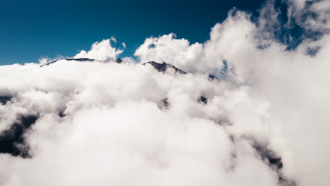 Drone-Volando-Sobre-Nubes-Blancas-Que-Cubren-La-Cima-Del-Monte-Agung-Con-Cielo-Azul-En-El-Fondo,-Volcán-Activo-En-Bali,-Indonesia