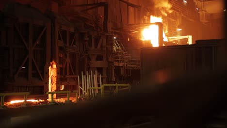 Intense-night-scene-at-an-industrial-steel-foundry,-flames-lighting-up-the-facility