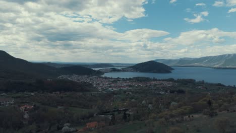 Drone-reveal-shot-above-a-village-on-a-hill,-red-roof-tops,-little-houses,-sunny-weather,-blue-water-lake,-SCENIC-mountains,-4K-video