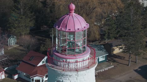 A-quaint-lighthouse-with-a-striking-pink-top,-nestled-in-lush-greenery-on-a-sunny-day,-aerial-view