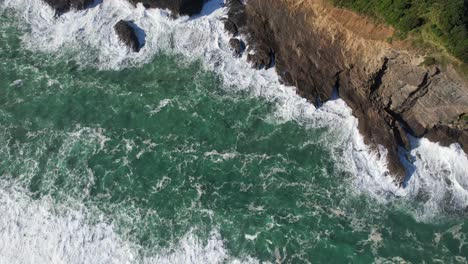 Overhead-View-of-Waves-Crashing-On-Rugged-Coast-Of-Piha-Beach-In-Auckland,-New-Zealand
