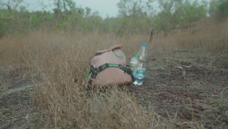 Abandoned-backpack-and-water-bottles-in-dry-grass-under-overcast-sky,-evoking-themes-of-travel-and-solitude