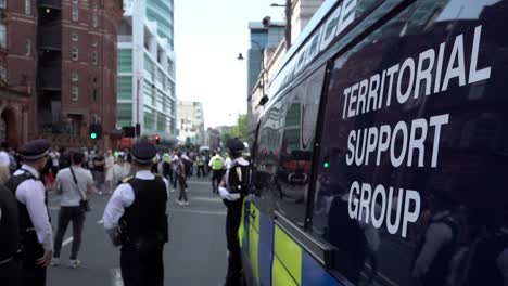 Un-Grupo-De-Agentes-De-La-Policía-Metropolitana,-Incluido-Un-Inspector-Jefe,-Se-Encuentra-Junto-A-Una-Furgoneta-Antidisturbios-Del-Grupo-De-Apoyo-Territorial-Azul-Oscuro-Mientras-Otros-Agentes-Limpian-La-Carretera-Durante-Un-Evento-De-Orden-Público.