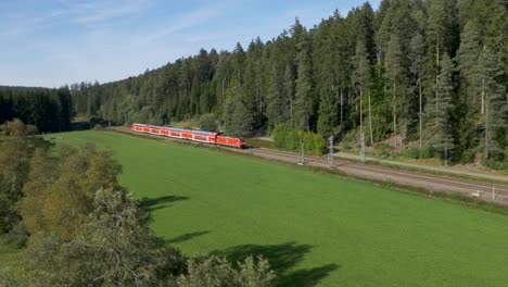 Ein-Leuchtend-Roter-Zug-Der-Deutschen-Bahn-Rast-Durch-Eine-üppig-Grüne-Landschaft,-Luftaufnahme