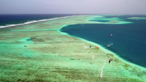 Vibrant-kite-surfers-at-los-roques-barrier-reef-with-turquoise-waters,-aerial-view