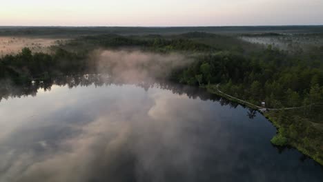 Flyover-of-reflective-foggy-Paukjarv-Lake-in-Estonia-at-golden-sunrise