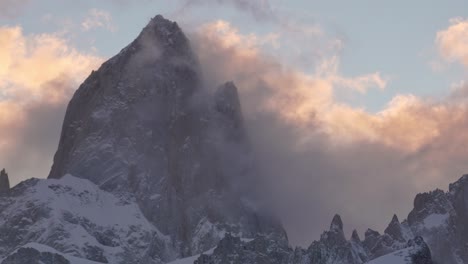 Mountain-peak-Fitz-Roy-surrounded-by-swirling-clouds-during-a-vibrant-sunset,-showcasing-nature's-grandeur