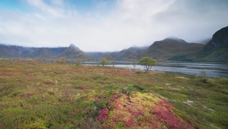 Low-clouds-whirl-and-pass-above-the-fjord-and-autumn-valley-surrounded-by-mountains-in-a-timelapse-video