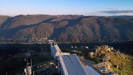 Tilt-aerial-reveal-of-empty-ski-slope-chairlift-in-summer-with-Thredbo-town-in-background,-Snowy-Mountains,-NSW,-Australia