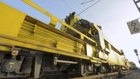 Maquinaria-Ferroviaria-Amarilla-Especializada-Que-Trabaja-En-Las-Vías-Durante-El-Día,-Filmada-Bajo-La-Luz-Del-Sol-Vibrante
