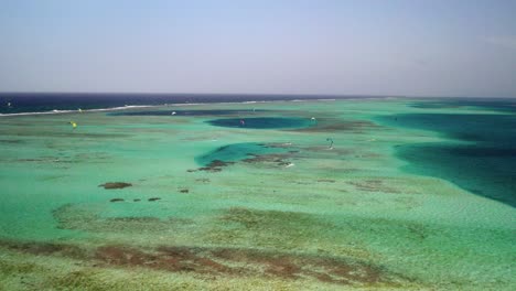 Kite-surfers-gliding-over-vibrant-coral-reefs-in-clear-turquoise-waters,-daytime,-aerial-view