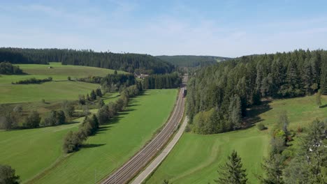 Un-Tren-Que-Pasa-Por-Un-Exuberante-Paisaje-Verde-Con-Colinas-Boscosas,-Vista-Aérea