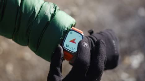 Hand-Mit-Handschuh-Prüft-Geografische-Koordinaten-Und-Position-Auf-Dem-Kompass-Des-Apple-Watch-Ultra-Touchscreens-Mit-Orangefarbenem-Silikonband