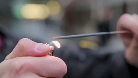 Close-up-of-a-sparkler-being-ignited-by-a-person-in-blurred-urban-background