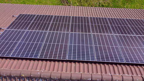 Paneles-Solares-De-Consumo-Sobre-Techo-De-Tejas-Rojas,-Hierba-Verde-Y-árboles-Alrededor-De-La-Residencia,-Antena-Dolly