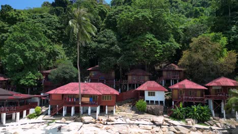 Island-Hill-Huts-in-lush-Jungle-fores,-emerald-waters-lagoon