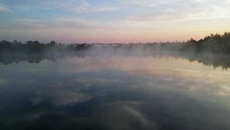 Flyover-lone-conifer-tree-to-small-foggy-lake-reflecting-sunrise-sky